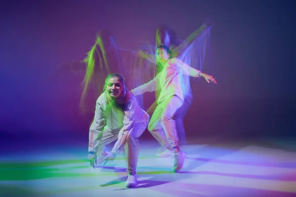 stock image Portrait of young girls dancing hip-hop isolated over gradient blue purple background in neon with mixed light. Concept of movement, youth culture, active lifestyle, action, street dance, hobby