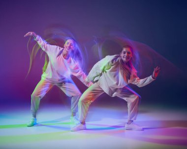 Hip-hop dansı yapan genç kızlar, sahnede sahne alarak, karışık ışıkla karışık mavi bir arka planda izole edilmiş bir şekilde. Hareket kavramı, gençlik kültürü, aktif yaşam tarzı, aksiyon, sokak dansı
