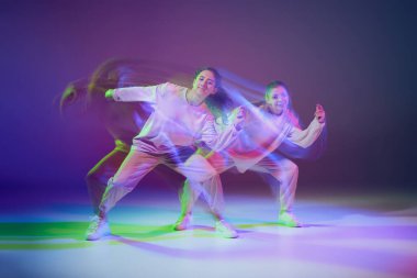 Hip-hop dansı yapan genç kızların portresi karışık ışıkla karışık mavi mor arka planda izole edilmiş. Enerji patlaması. Hareket kavramı, gençlik kültürü, aktif yaşam tarzı, aksiyon, sokak dansı