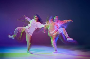 Hip-hop dansı yapan genç kızların portresi karışık ışıkla karışık mavi mor arka planda izole edilmiş. Eğlence. Hareket kavramı, gençlik kültürü, aktif yaşam tarzı, aksiyon, sokak dansı