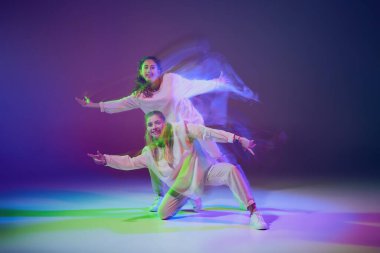 Hip-hop dansı yapan genç kızların portresi karışık ışıkla karışık mavi mor arka planda izole edilmiş. Mutluluk. Hareket kavramı, gençlik kültürü, aktif yaşam tarzı, aksiyon, sokak dansı