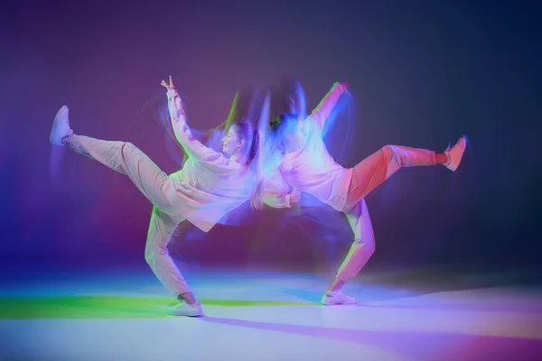 2人の若い女の子が ネオンのグラデーションの青紫色の背景に 混合光で孤立したヒップホップを踊っています よく調整されている 若者文化 アクティブライフスタイル アクション ストリートダンスの概念 — ストック写真