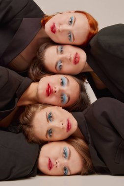 Siyah ceketli, parlak makyajlı genç ve güzel kadınlar gri arka planda kafa üstü yatıyorlar. Güzellik kavramı, özgürlük, duygular, sıradışı moda, modern tarz, gençlik