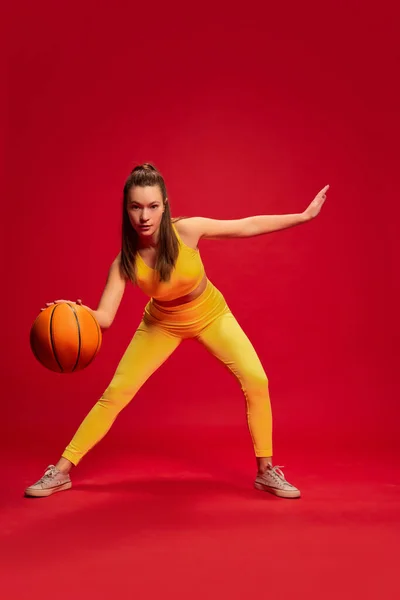 穿着黄色运动服的年轻女子的画像 她摆姿势 打篮球 在红色的背景下独自流口水 青年文化 面部表情 生活方式 健康的概念 — 图库照片