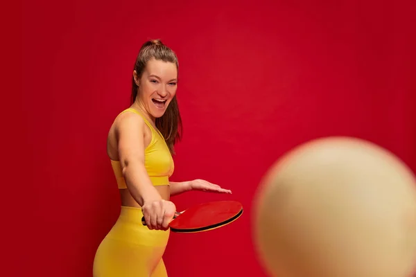 黄色のスポーツウェアのポーズで若い女性の肖像画 赤の背景に孤立卓球を再生します 青少年文化 スポーツ ライフスタイル 余暇の概念 — ストック写真