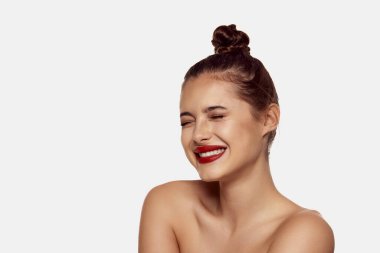 Saçları topuz ve kırmızı dudaklarıyla beyaz arka planda poz veren güzel bir kız. Mükemmel gülümseme. Diş beyazlatma. Diş bakımı. Güzellik kavramı, cilt bakımı, kozmetoloji, estetik cerrahi, makyaj