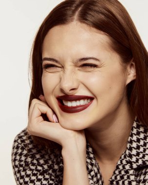 Şık bir ceketle poz veren güzel bir kızın yakın plan portresi ve beyaz arka planda izole edilmiş neşeli bir gülümseme. Güzellik, cilt bakımı, kozmetoloji, estetik cerrahi, makyaj, moda kavramı