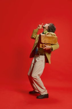 Kırmızı arka planda izole edilmiş klasik takım elbiseli, bıyıklı şık bir adamın portresi. Şans dilemek için dua ediyorum. Retro biçim kavramı, istihdam, duygular, yüz ifadesi, meslek