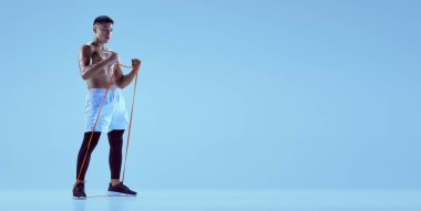 Genç kaslı adam eğitiminin portresi spor genişleticisi ile mavi arka planda izole edilmiş neon ışıkta. El ilanı resmi. Spor anlayışı, fitness, sağlıklı ve aktif yaşam tarzı, motivasyon, egzersiz