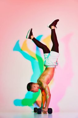 Pembe arka planda neon ışıkta izole edilmiş dambıllarla elleri birbirine dolanan genç kaslı adamın portresi. Çok renkli bir gölge. Spor, fitness, sağlık, aktif yaşam tarzı, motivasyon, egzersiz kavramı