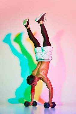 Genç kaslı adam eğitimi, pembe arka planda neon ışıkta izole edilmiş dambıllarla el ele tutuşmak. Çok renkli bir gölge. Spor anlayışı, fitness, sağlıklı ve aktif yaşam tarzı, egzersiz