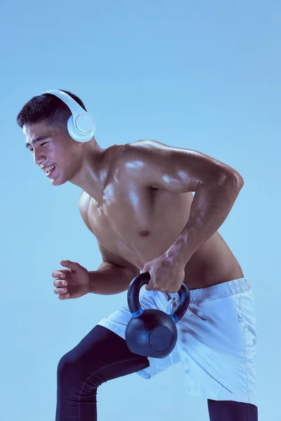 ヘッドフォンでの若い筋肉の男のトレーニングの肖像画 ネオンライトの青の背景に隔離された重量を持ち上げる スポーツ フィットネス 健康的で活動的なライフスタイル モチベーション ワークアウトの概念 — ストック写真