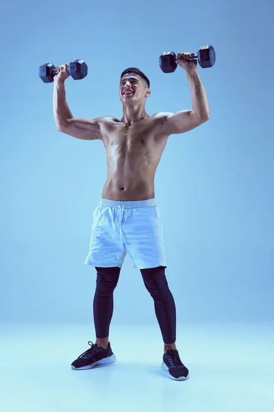 Portret Młodego Muskularnego Mężczyzny Trenującego Podnoszącego Hantle Niebieskim Tle Neonowym — Zdjęcie stockowe