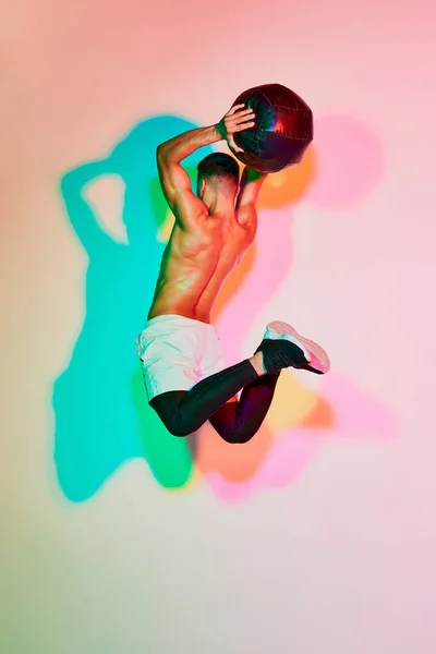年轻的肌肉男训练与医疗球在一个跳跃隔离粉红背景的霓虹灯 五彩斑斓的阴影 健康和积极的生活方式 锻炼的概念 — 图库照片