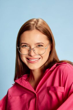 Mavi arka planda izole edilmiş pembe elbiseli güzel bir kızın portresi. Doğal makyaj görünüşü. Gençlik kavramı, güzellik, moda, yaşam tarzı, duygular, yüz ifadesi. Ad