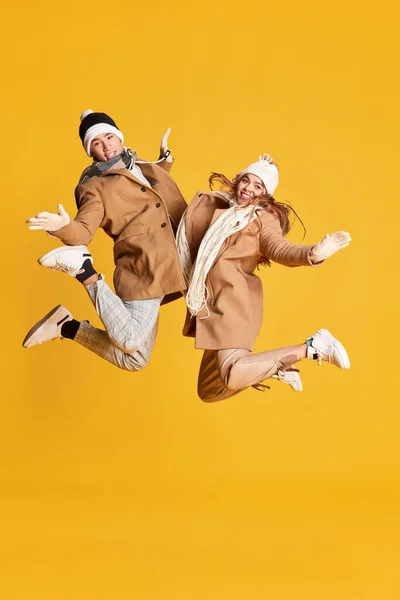 stock image Portrait of stylish young man and woman in winter clothes cheerfully posing, jumping isolated on yellow background. Concept of emotions, winter holidays, fashion, lifestyle, celebration, relationship