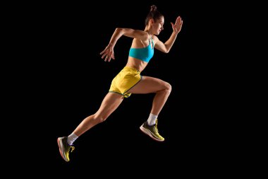Genç sportif kadın, koşucu ve koşucu siyah arka planda izole edilmiş hareket halinde mavi-sarı renkli spor giyim giyiyor. Koşu tekniği. Spor, spor, enerji, hareket kavramı