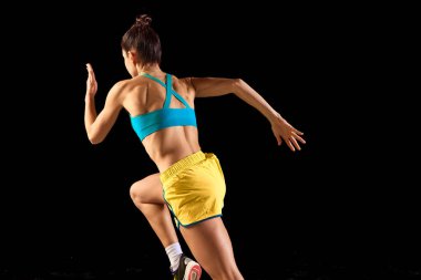 Arkadan bak. Genç sportif kadın, koşucu ve koşucu siyah arka planda izole edilmiş hareket halinde mavi-sarı renkli spor giyim giyiyor. Koşu tekniği. Spor, spor, enerji, hareket kavramı