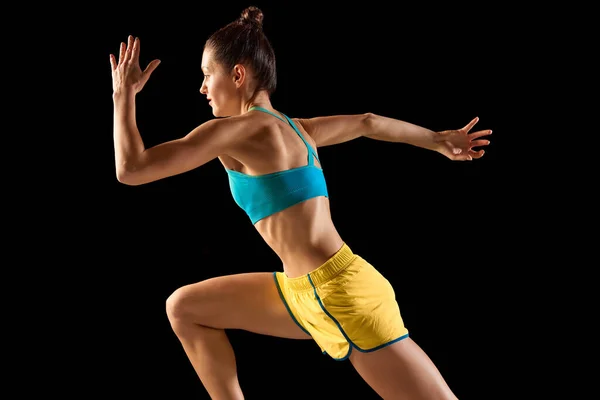 年轻的女运动健将 跑步者和慢跑者穿着蓝色 黄色的运动鞋 在运动动作上与黑色背景隔离 跑技术 运动概念 — 图库照片