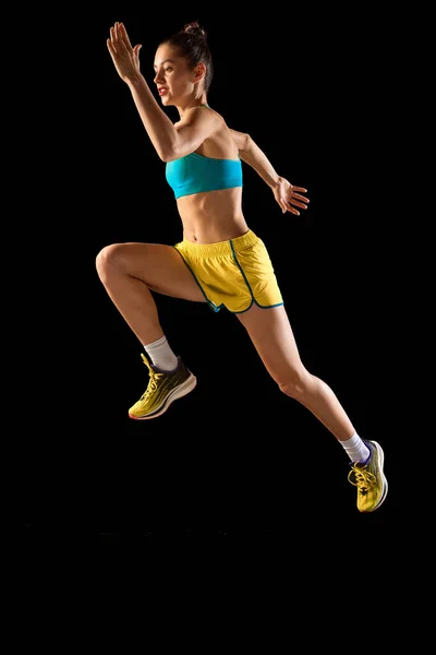 一个穿着运动服的女运动员跳得很高 被黑色背景隔开了 体育的概念 年轻的运动员 跑步者看起来很有动力 很集中 — 图库照片