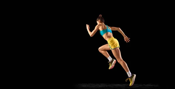女运动员在行动 身穿蓝黄色运动服的年轻的健身女运动员跑步 在黑暗的背景下进行训练 动态运动 跑步技巧 — 图库照片