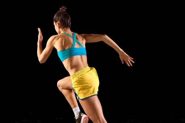 バックビュー ブラックを基調とした動きの中にブルーイエローのスポーツウェアを身に着けた若い女性 ランナー ジョガー ランニングテクニック スポーツ フィットネス エネルギー 運動の概念 — ストック写真