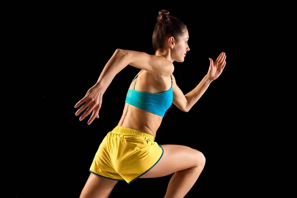 年轻的女运动健将 跑步者和慢跑者穿着蓝色 黄色的运动鞋 在运动动作上与黑色背景隔离 跑技术 运动的概念 — 图库照片