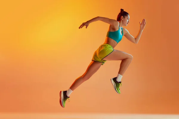 运动员在运动 穿着运动服跑步的年轻健康的女运动员 在霓虹灯下在黄色背景上进行训练 动态的动作 跑技术 侧视图 — 图库照片