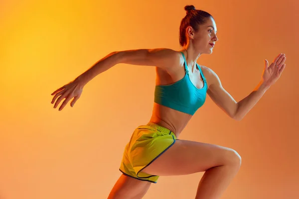 运动员在运动 穿着运动服跑步的年轻健康的女运动员 在霓虹灯下在黄色背景上进行训练 动态的动作 跑技术 — 图库照片