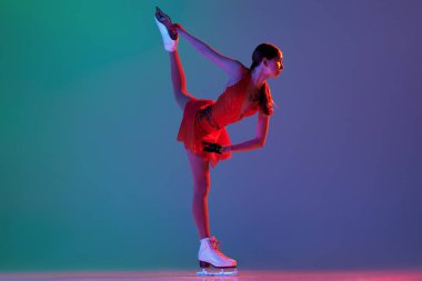 Kış sporları. Kırmızı sahne kostümlü genç bir bayan artistik patinajcı temel buz pateni elementlerini gösteriyor. Neon ışıklarıyla yeşil-mavi arkaplan üzerinde izole edilmiş hareketler. İlan için alanı kopyala
