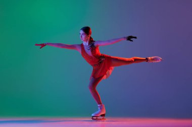 Genç sporcu kız, kırmızı sahne kostüm giyen genç bayan artistik patinajcı neon renkli yeşil-mavi arka planda izole edilmiş. Hareket halindeki bir sporcu. Spor, güzellik, kış sporları. İlan için alanı kopyala