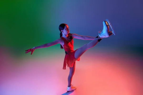 Winter sports. One junior female figure skater in red stage costume showing base figure skating elements, movements isolated over gradient green-blue background in neon light. Copy space for ad