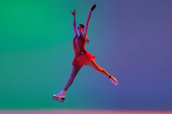 ウィンタースポーツ ベースフィギュアスケートの要素を示す赤いステージの衣装を着た若い女性フィギュアスケート選手の1人 ネオンライトでグラデーションの緑青の背景に隔離された動き 広告のコピースペース — ストック写真