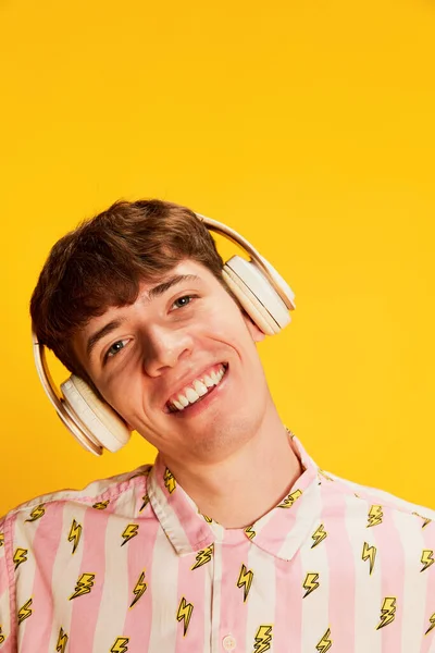 ヘッドフォンの笑顔で感情的な若い男のクローズアップ肖像画 明るい黄色の背景の上に隔離された音楽を聞いて 若者文化 肯定的な感情 楽しそうだな — ストック写真