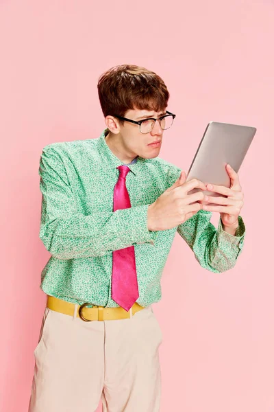 タブレットを使ってる 面白い感情的な男 ヴィンテージスタイルのシャツとズボンを着て学生オタクは 明るいピンクの背景に隔離された楽しみを持っています 楽しさ スタイル ファッション ポジティブで奇妙な感情 — ストック写真