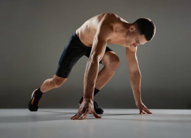 Başlangıçta. Sportif adam, kaslı atlet, koşucu hareket halinde bisiklet şortu giyiyor ve gri arka planda izole edilmiş hareket ediyor. Enerji, hız, spor ve güzellik, motivasyon, başarı kavramı.