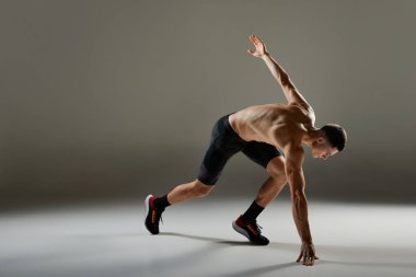 Sportif adam, kaslı atlet, koşucu hareket halinde bisiklet şortu giyiyor ve gri arka planda izole edilmiş hareket ediyor. Enerji, hız, spor ve güzellik kavramı.