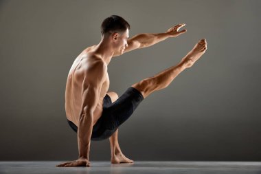 Gri arka planda izole edilmiş hayvan akışı spor unsurları gösteren esnek erkek sporcu portresi. Yoga, fitness, moda sporlar, vücudun güzelliği. İnsan vücudunun zerafeti ve esnekliği