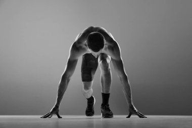 Güç ve enerji. Kaslı atlet, başlangıç çizgisinde koşucu gri arka planda izole edilmiş. Spor ve güzellik konsepti. Siyah beyaz portre. Tek renkli olsun. Motivasyon, başarı kavramı.