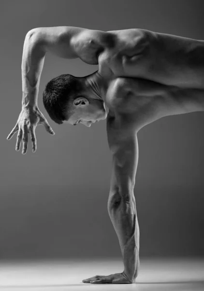 Cropped black and white footage of male muscular body doing hand stand isolated over gray background. Yoga, fitness, trendy sports, beauty. Grace and flexibility of human body