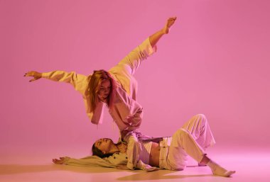 İki şık bayan dansçı gündelik kıyafetlerle dans ediyor çağdaş koreografi dansı kristal pembe arka planda izole edilmiş. Modern sanat kavramı, yaratıcılık, füzyon. Hareketlerdeki duygular