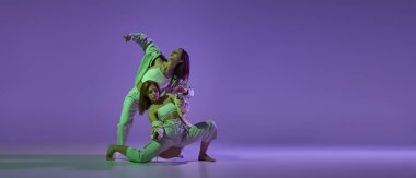 Deneysel dans. İki genç kız hareket halinde, hareket mor arka planda izole edilmiş. Yeni dans stili kavramı, gençlik kültürü, müzik ve moda, reklam, trendler. Esnek ve zarif dansçılar.