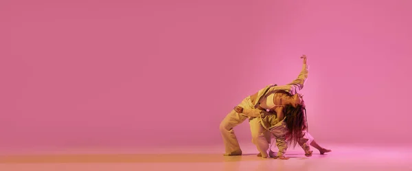 モダンダンスアート 若い女の子 スポーツスタイルの服のダンサーのカップルはネオンで淡いピンクの背景に隔離された実験的なダンスを踊る ダンスの概念 広告のコピースペース — ストック写真