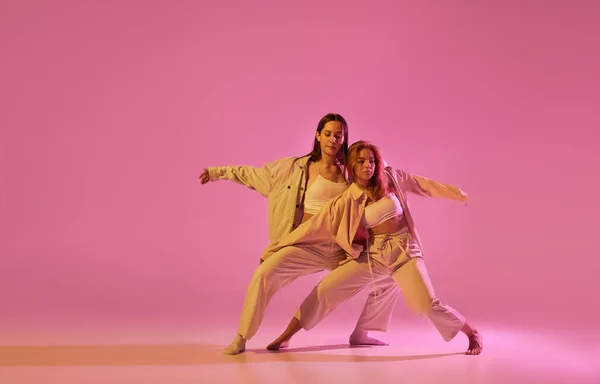 ピンクのクリスタルを背景に現代的な振付ダンスを踊るカジュアルなスタイルの服を着た2人のスタイリッシュな女性ダンサー 現代美術の概念 創造性 動きの中の感情 — ストック写真