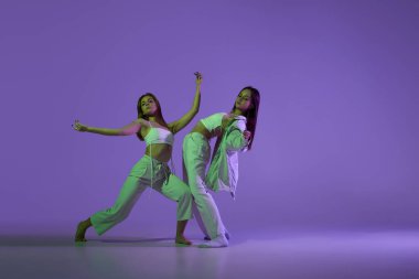 Dans eden genç kızların stüdyo görüntüleri. Şık bir performans. Mor arka planda izole edilmiş iki çağdaş dansta iki genç kadın. Yeni dans stili, gençlik, müzik ve moda, reklam, trendler.