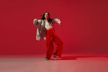 Hip-hop dansı yapan genç bir kızın dinamik portresi ya da koyu kırmızı arka planda izole edilmiş çağdaş dans. Deneysel dans. Müzik, dans, aktif yaşam tarzı, moda, tarz. Enerji ve esneklik