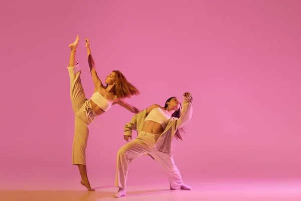 モダンダンスアート 若い女の子 スポーツスタイルの服のダンサーのカップルはネオンで淡いピンクの背景に隔離された実験的なダンスを踊る ダンスの概念 広告のコピースペース — ストック写真