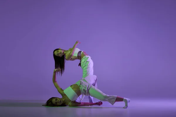 若い女の子のダンスのスタジオ映像 スタイリッシュなパフォーマンス 紫を背景にした表現力豊かなコンテンポラリーダンスの若い女性2人 新しいダンススタイル 音楽とファッション トレンド — ストック写真