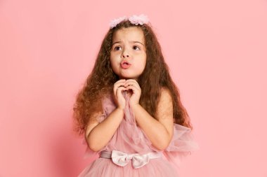 Çekici, küçük bir kızın portresi, pembe arka planda izole edilmiş uzun kıvırcık saçlı bir çocuk. Mutlu çocukluk, çocuk duyguları, moda ve reklam. Mutlu görünüyor, mutlu.