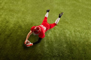 Amerikan futbolcusunun spor üniformalı ve yeşil çimen zemininde topu yakalayan koruyucu kasklı görüntüsü. Profesyonel spor, takım, yarışma, şampiyonluk kavramı